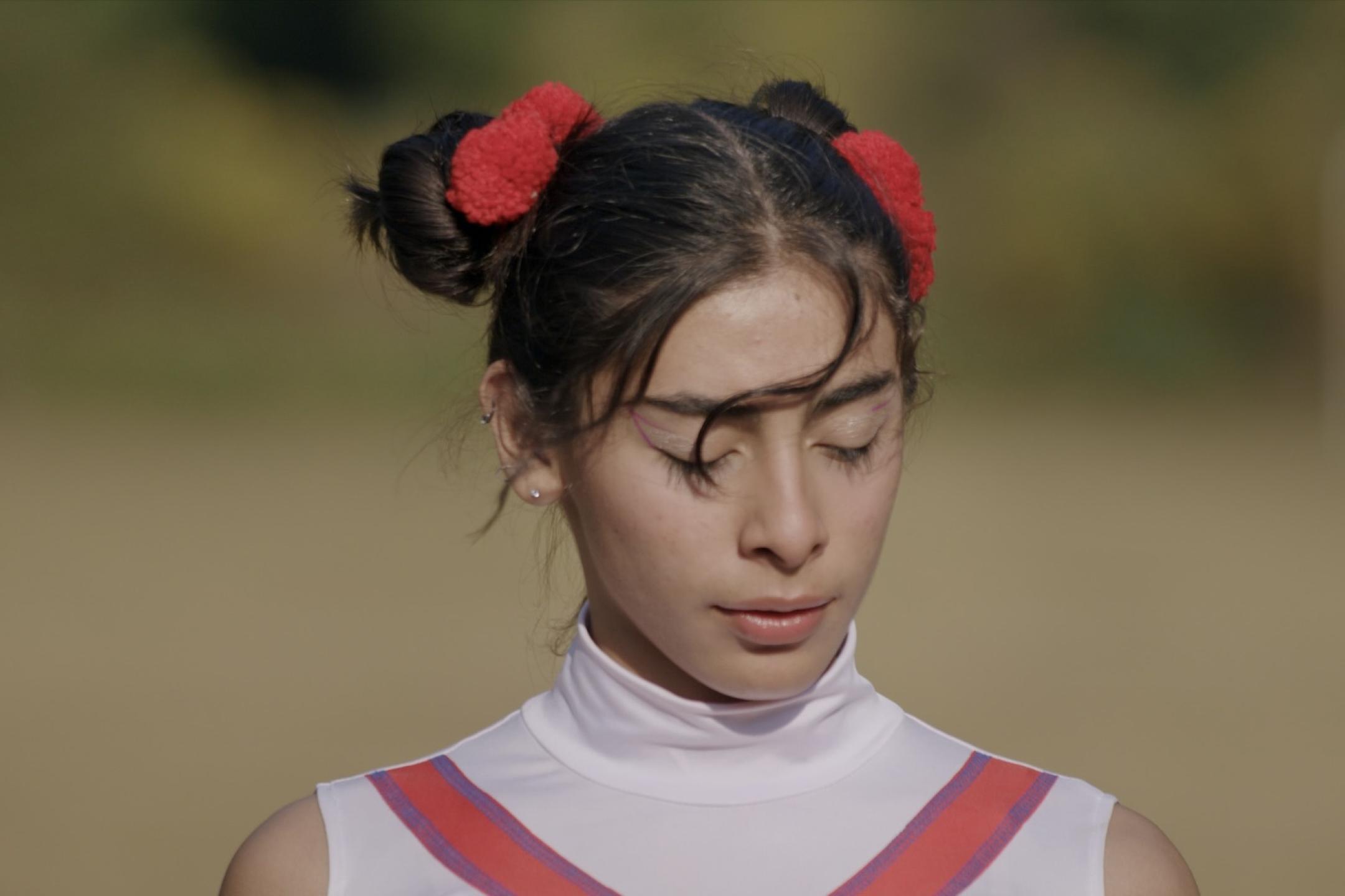 Ein Filmstill eines Mädchen mit zwei Dutts auf ihrem Kopf, sie hat die Augen geschlossen und ihr Pony weht im Wind