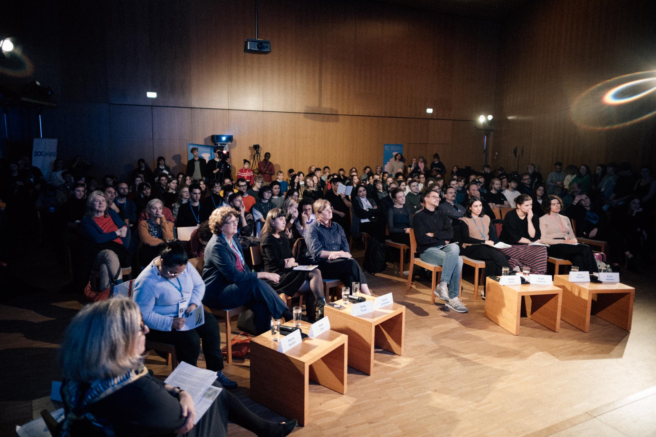 Eine große Gruppe sitzt auf Stühlen und schaut nach vorne
