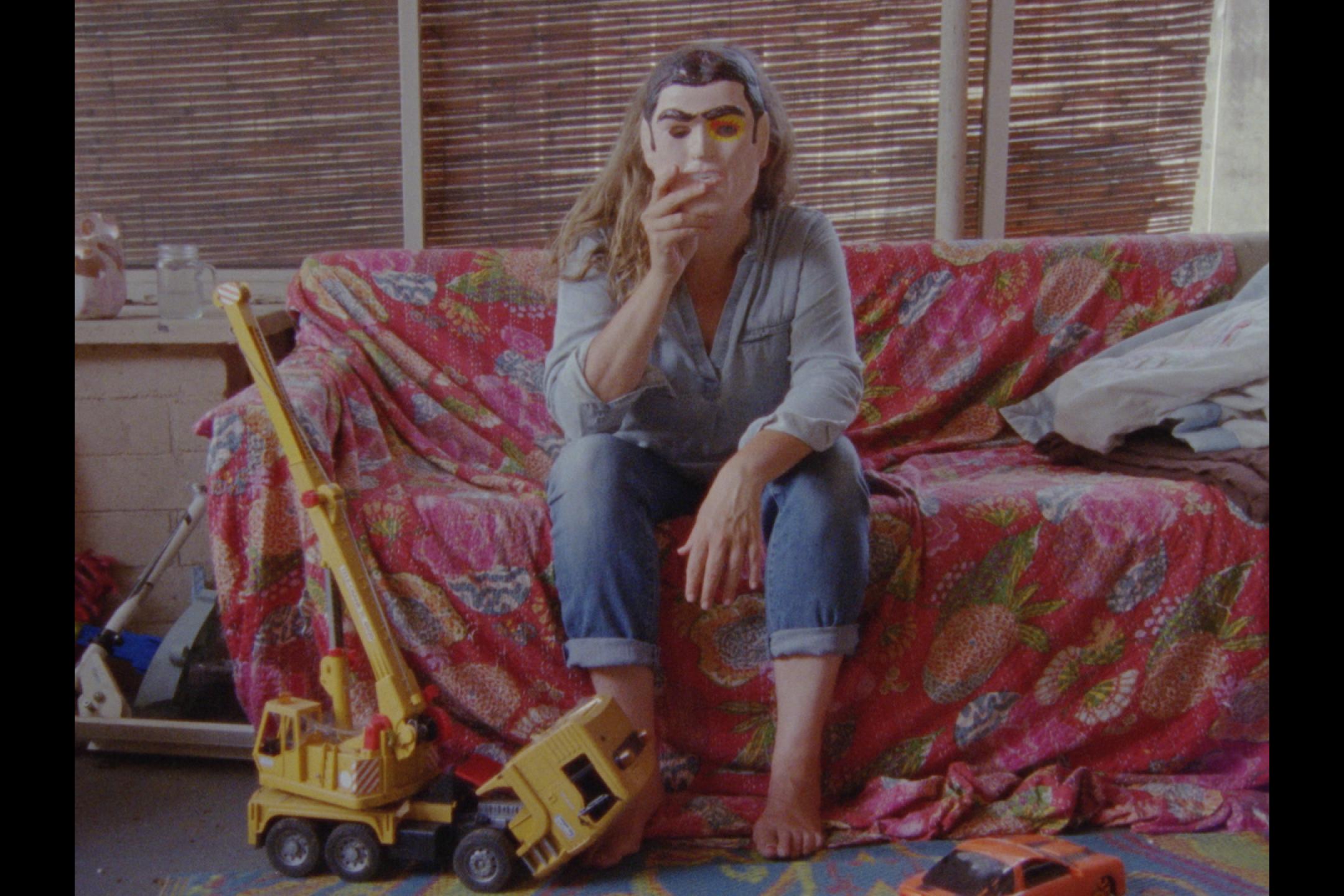 Lee Anne Schmitt sitzt auf einem Sofa  und hält sich eine Maske vors Gesicht