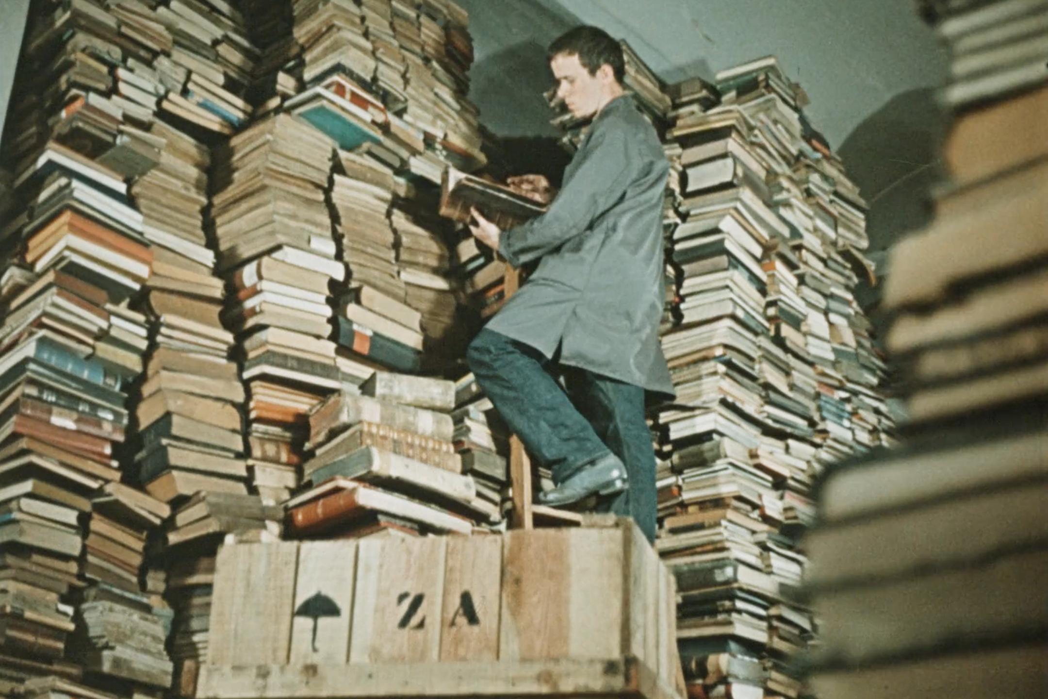 Mann steht auf einer Leiter in einem Raum mit riesigen Büchertürmen