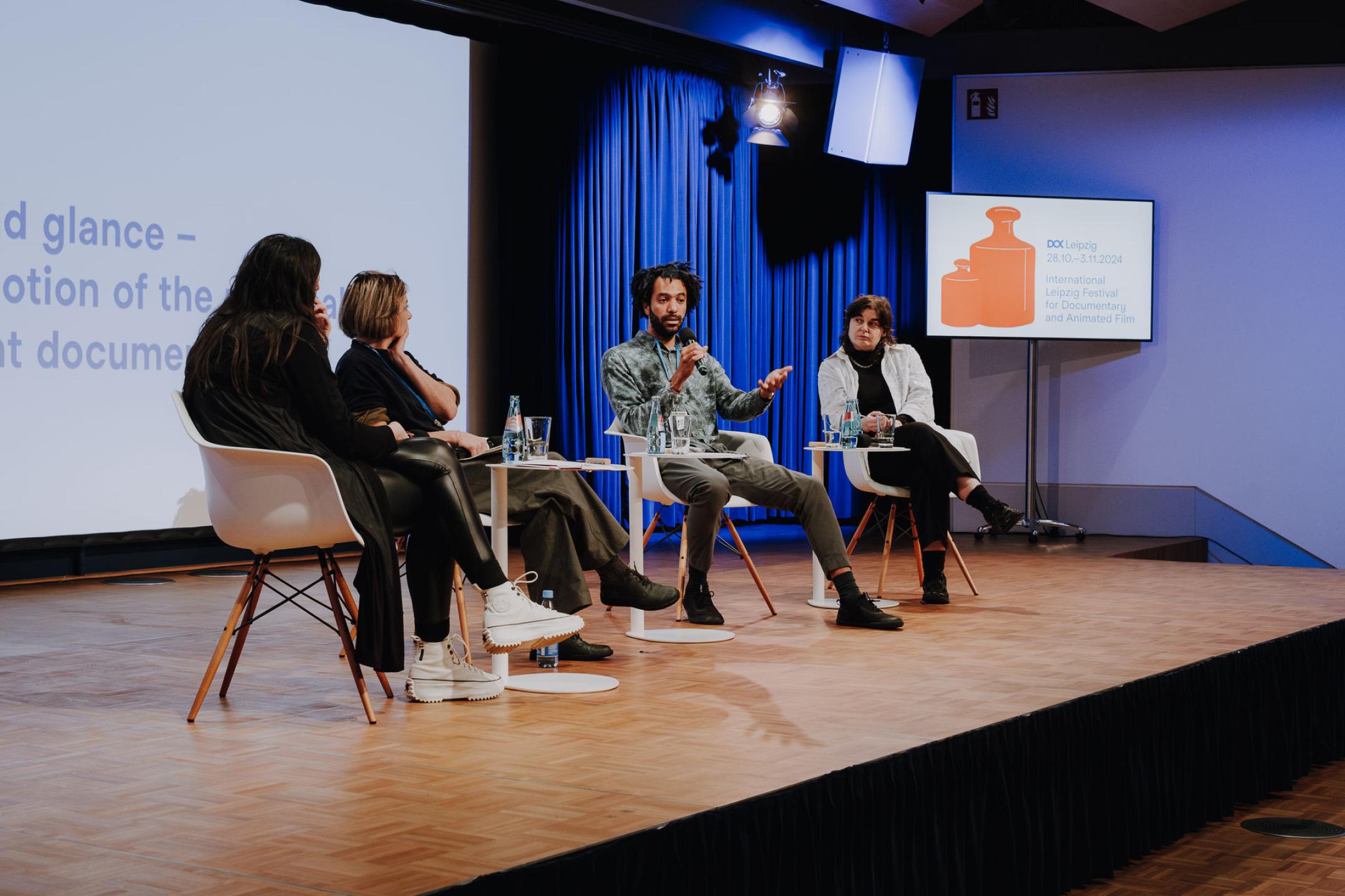 Vier Personen sitzen auf Stühlen auf einer Bühne