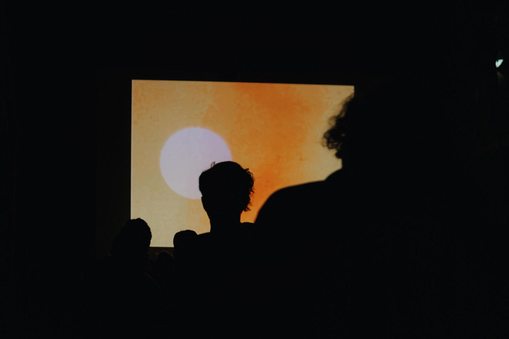 Umrisse von Menschen, die auf orangene Kinoleinwand schauen