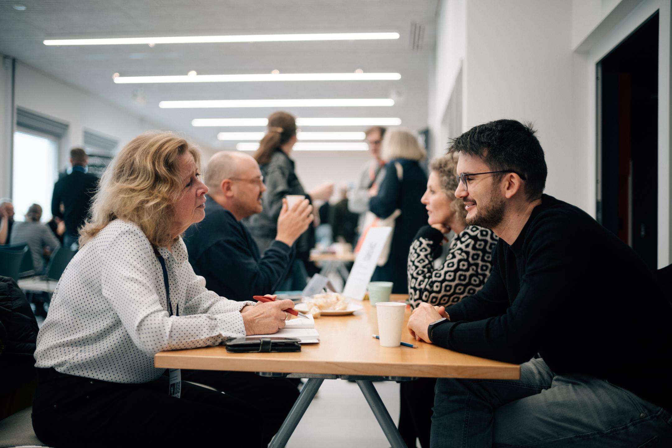 Personen sitzen sich an einem Tisch gegenüber