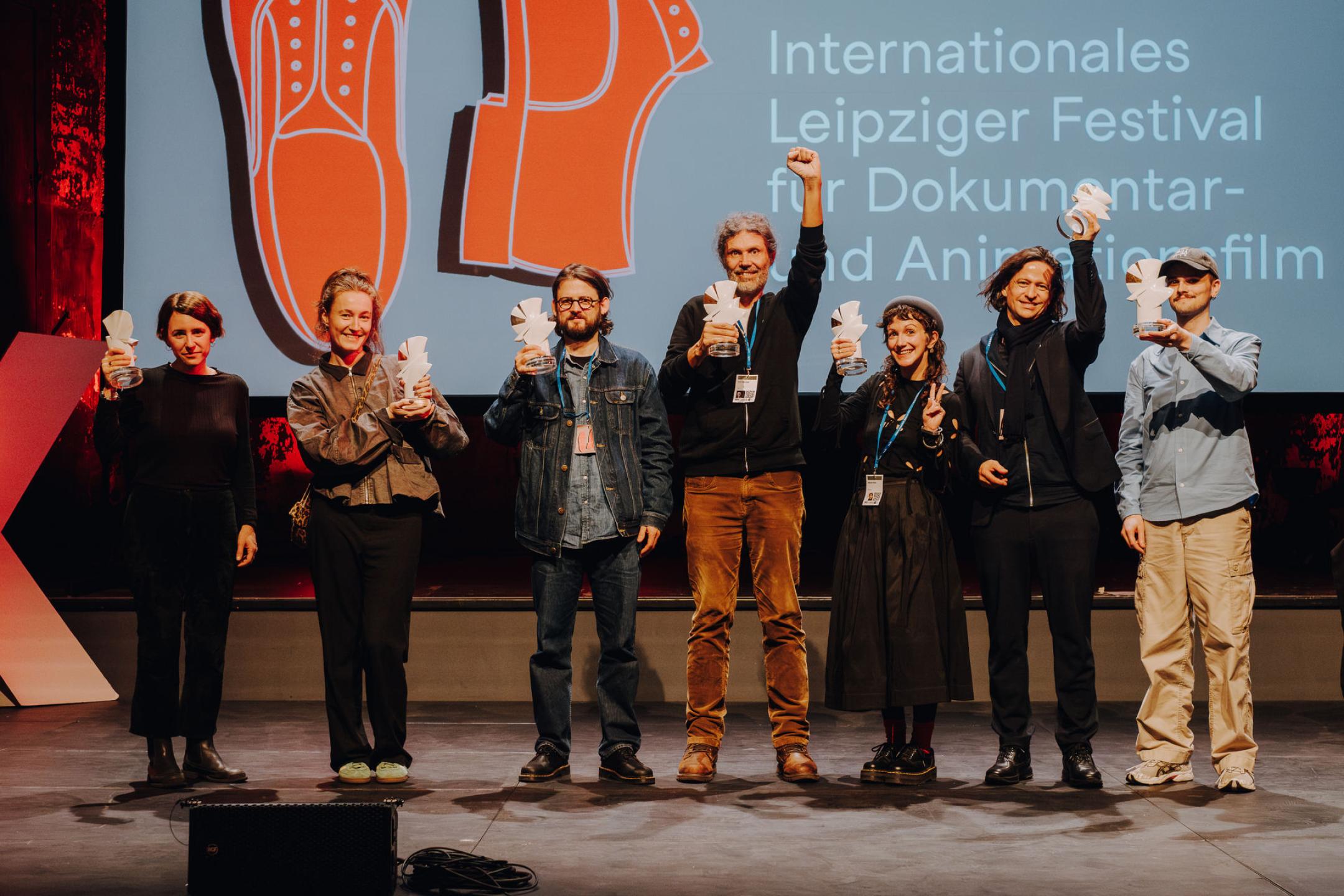 Gruppe von Personen auf Bühne, die ihre Tauben-Preise in die Luft halten