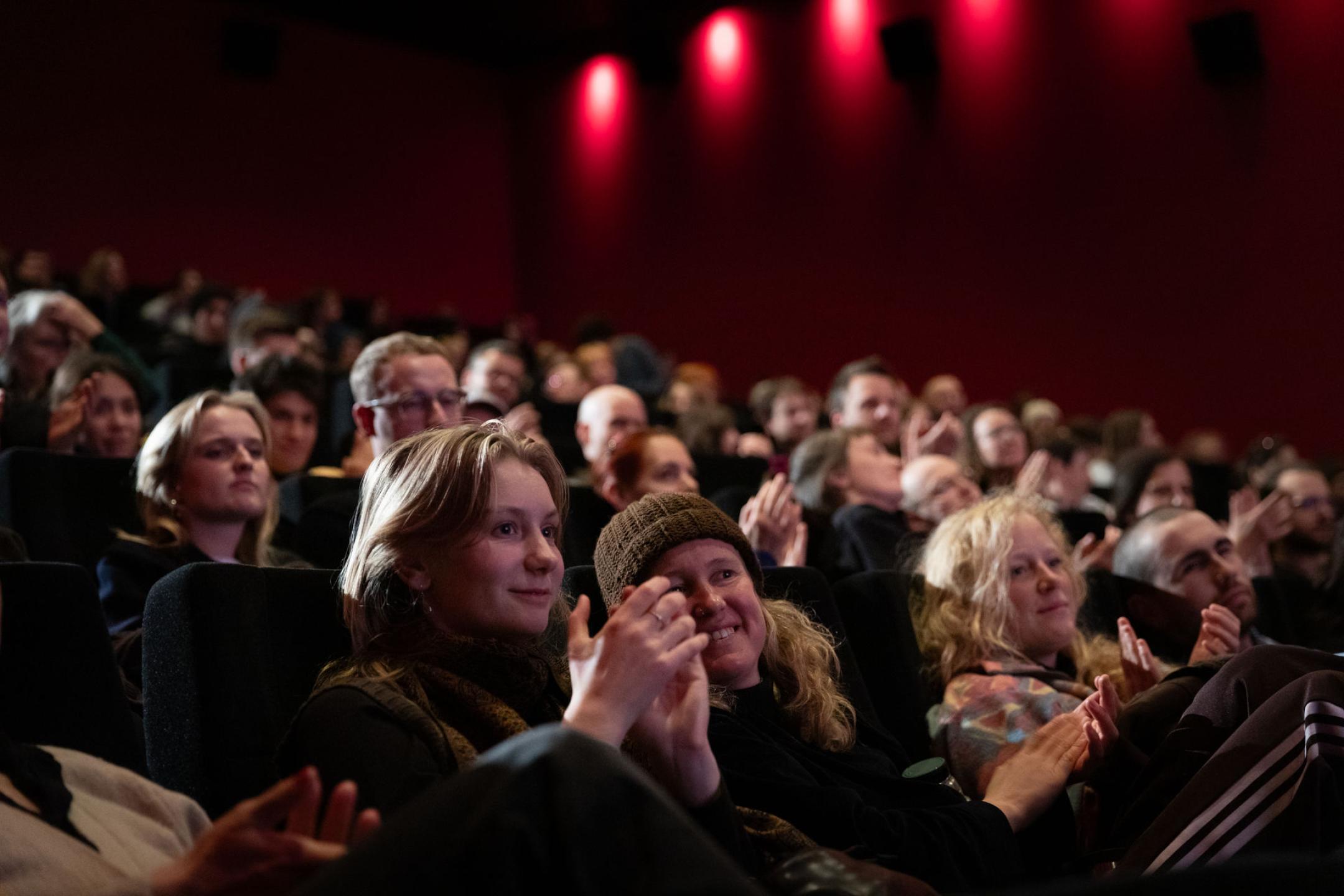 Ein Kinopublikum, im Vordergrund flüstern zwei Personen begeistert beim applaudieren