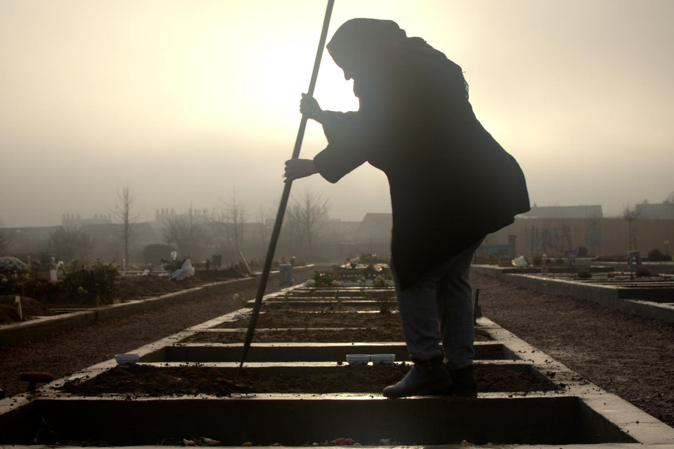 Die Silhouette einer Frau gegen die Sonne. Sie steht auf Gleisen und stochert mit einem Stab darin herum
