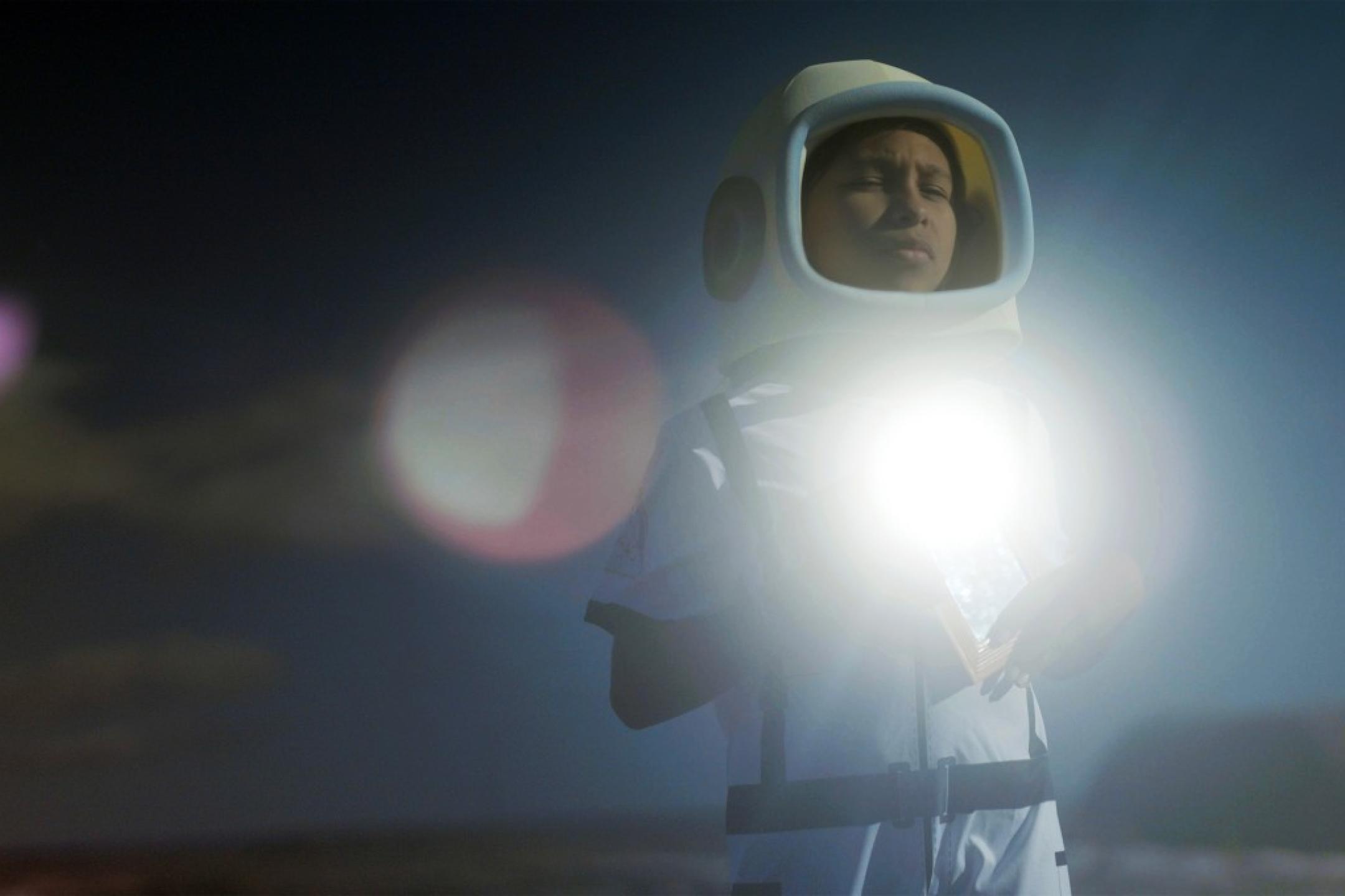 Ein Kind im Raumanzug hält ein gleißend helles Licht in den Armen und hält die Augen geschlossen