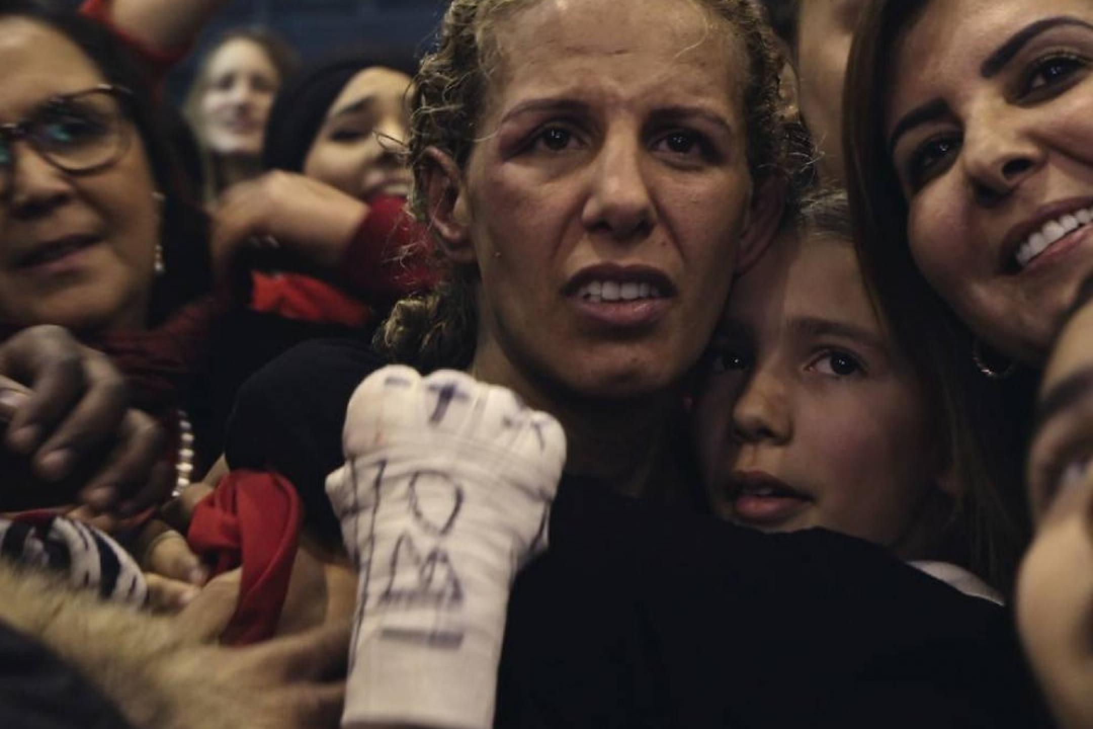 Boxerin mit emotionalem Gesichtsausdruck, die scheinbar nach einem Kampf von mehreren Frauen umgeben und von ihrer Tochter umarmt wird
