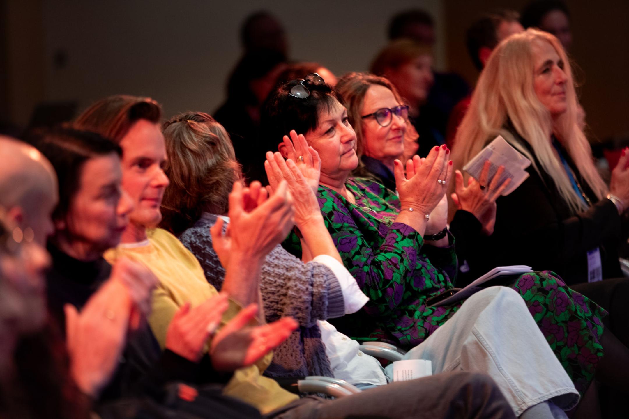 Eine Reihe an Menschen auf stühlen applaudiert wild