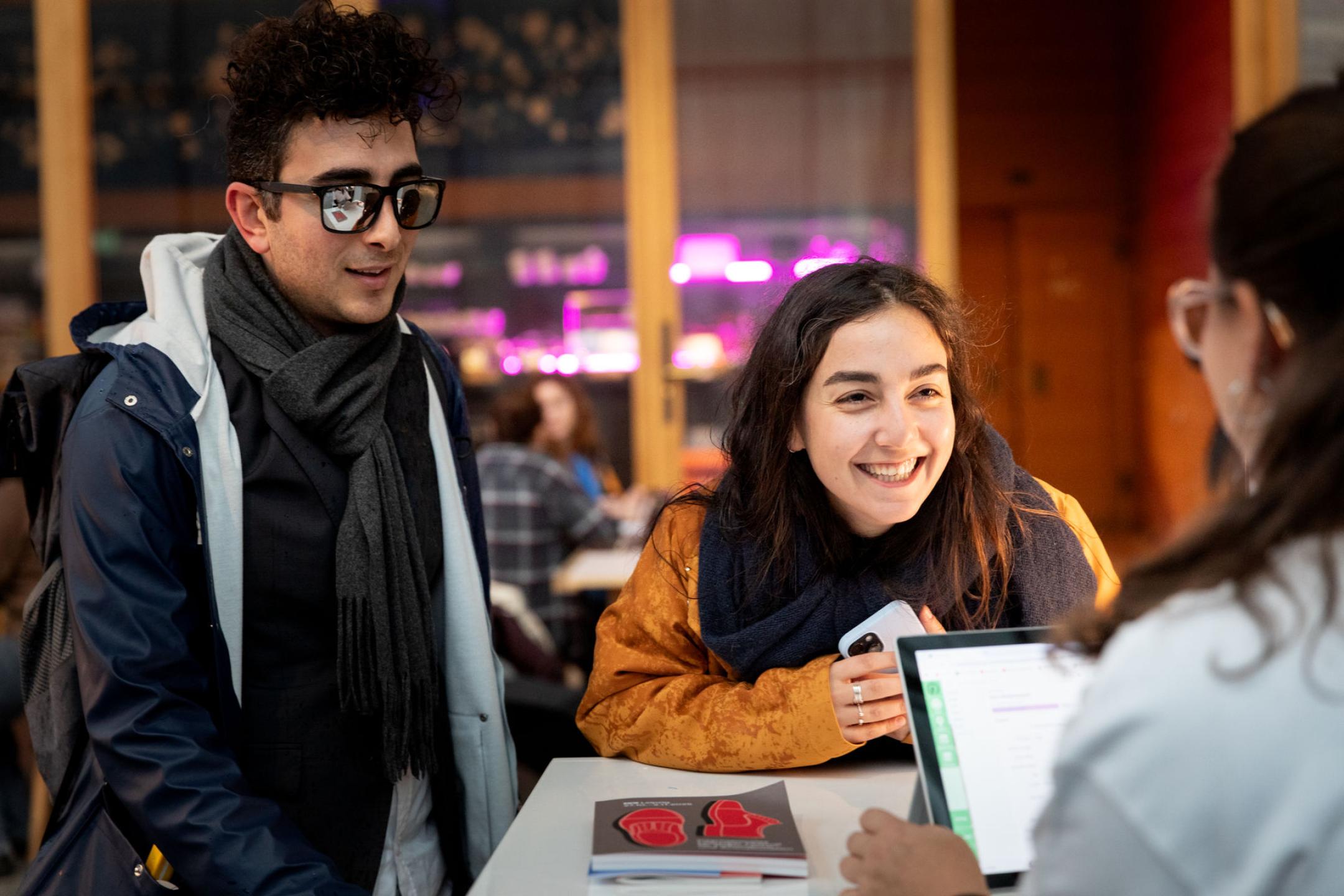 Eine junge Frau und ein junger Mann stehen an einem Counter. Vor ihnen liegt das DOK Leipzig Festival Programmheft.