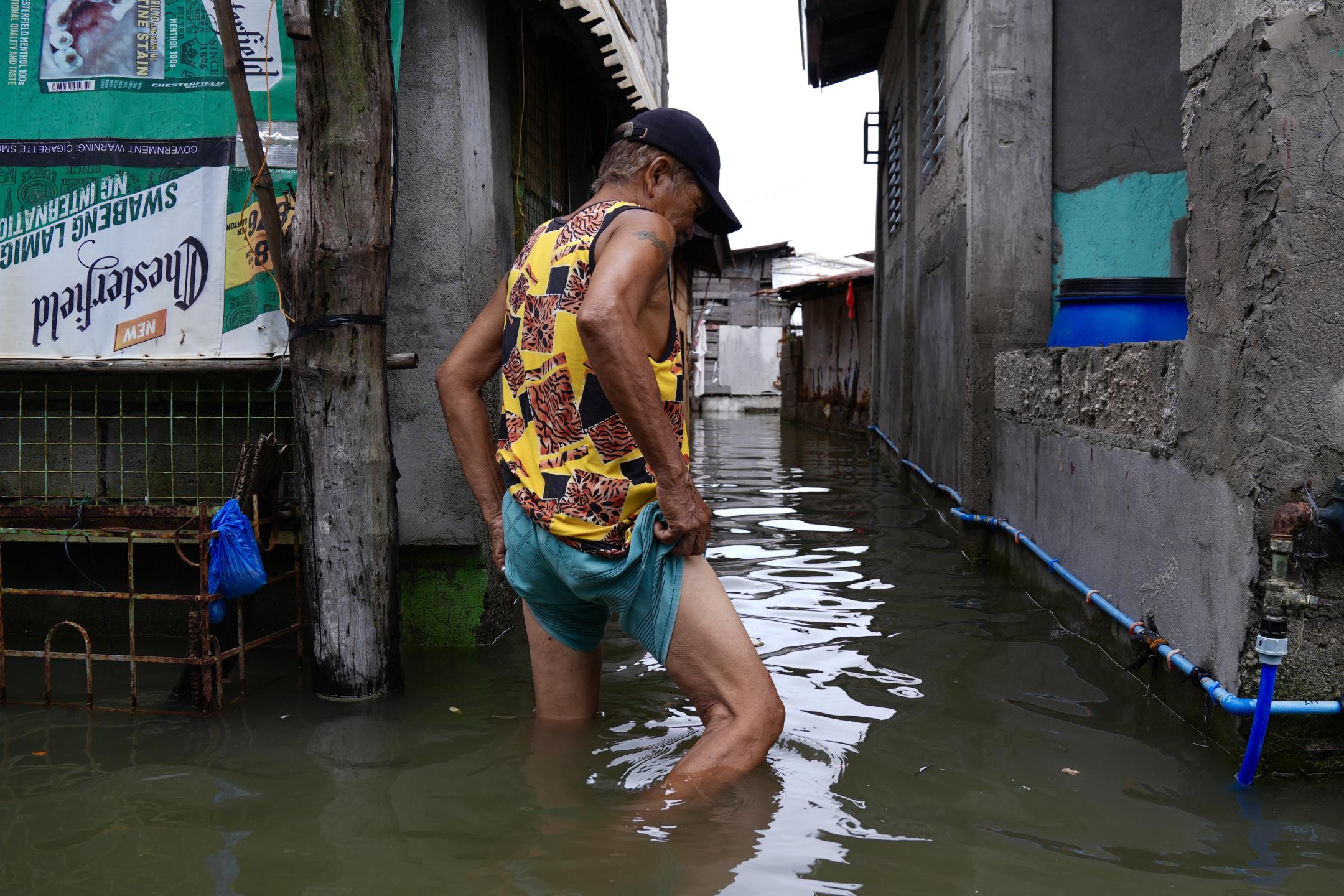 Ein Mann watet in kniehohem Wasser, das eine Straße zwischen engstehenden Häusern geflutet hat.