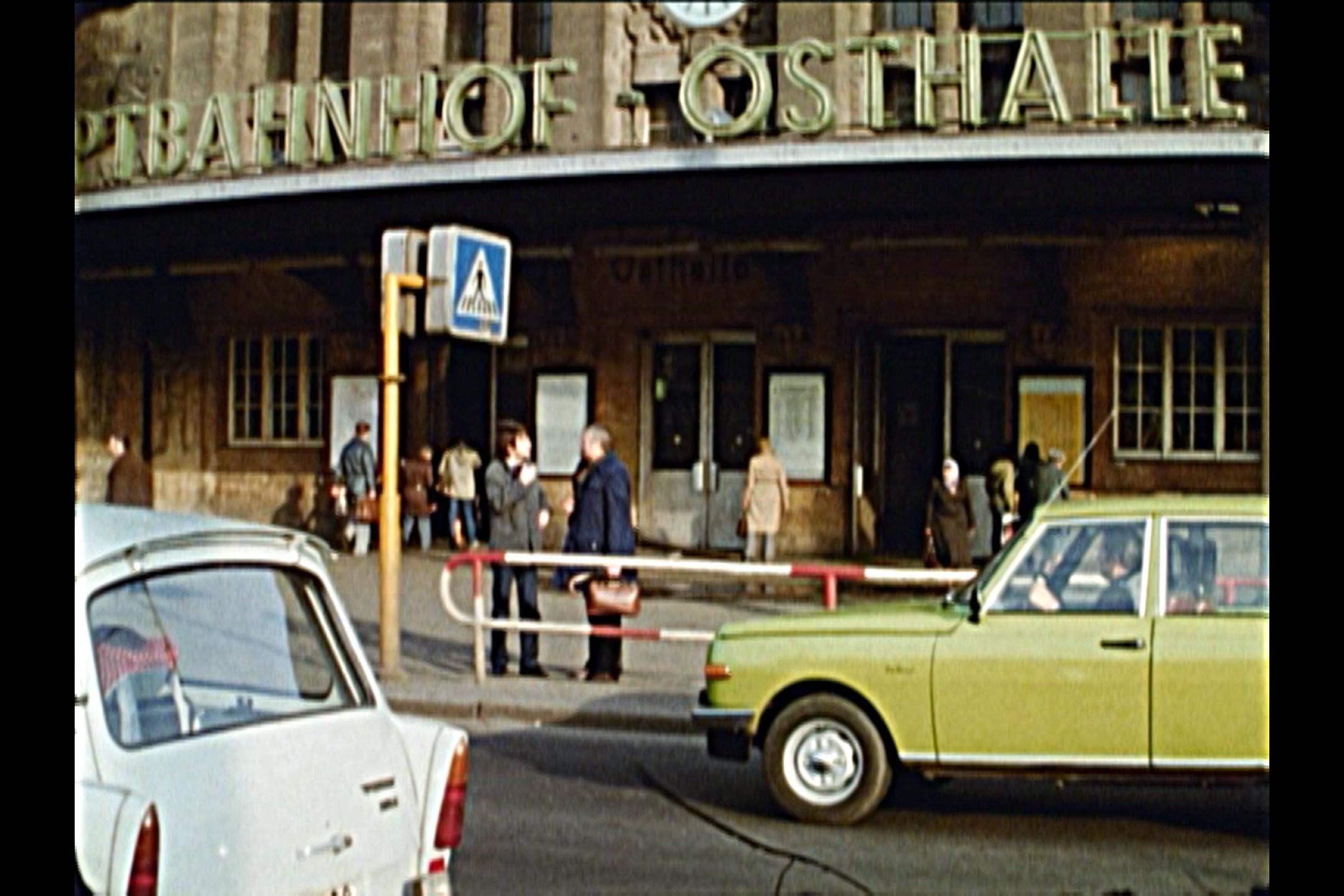 Analog wirkendes Bild vom Osteingang des Leipziger Hauptbahnhofs mit einem gelben Wartburg-Auto davor
