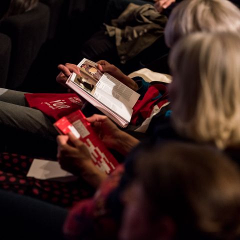 Zuschauerinnen in einer Kinoreihe lesen im DOK Leipzig Programmheft.
