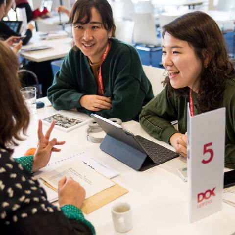 Three women are sitting around a text talking and laughing