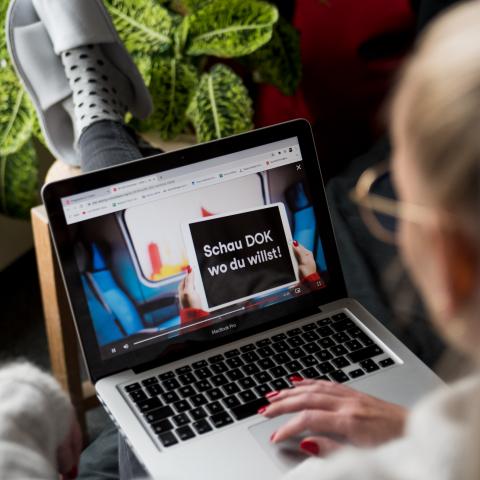 Blick über die Schulter einer Frau, die auf einen Laptop schaut, auf dem der DOK Leipzig Trailer läuft.