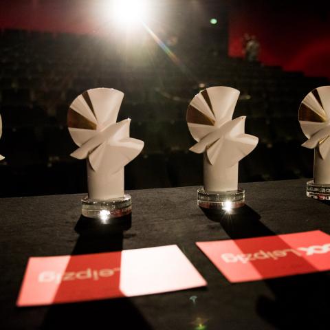 Mehrere Preisstatuen der Goldenen Tauben stehen nebeneinander auf einem Tisch, dahinter im Gegenlicht die Sitzreihen eines Kinosaals.