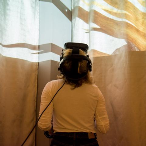 Ein weibliche Person mit VR-Brille legt ihren Kopf in den Nacken, oben im Bild erscheint eine Lichtinstallation.