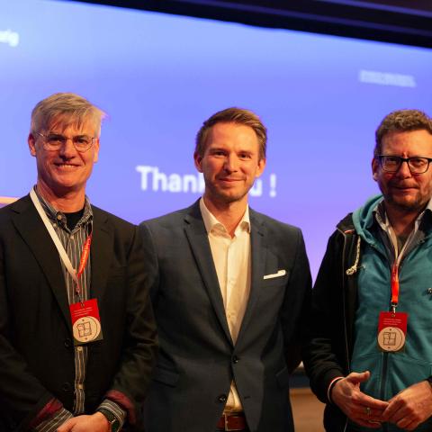Portrait of 3 male persons standing next to each other and all directly smiling to the camera.