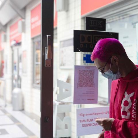 Vor einer Tür steht eine person mit knallig pinken haaren und einem Dok Pulli