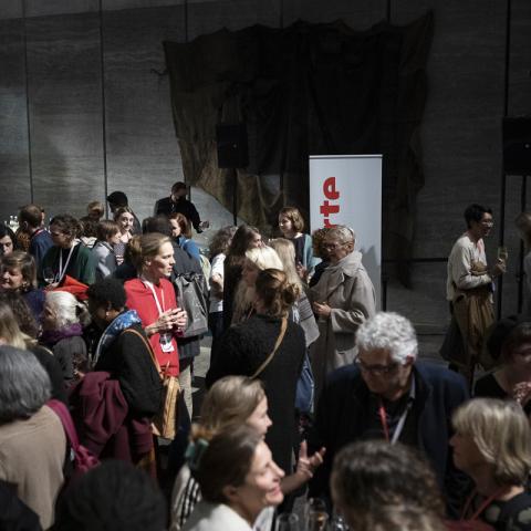 An evening event at the festival center at MdbK Leipzig: The lobby is crowded with people, standing in small groups at bar tables, talking to each other.
