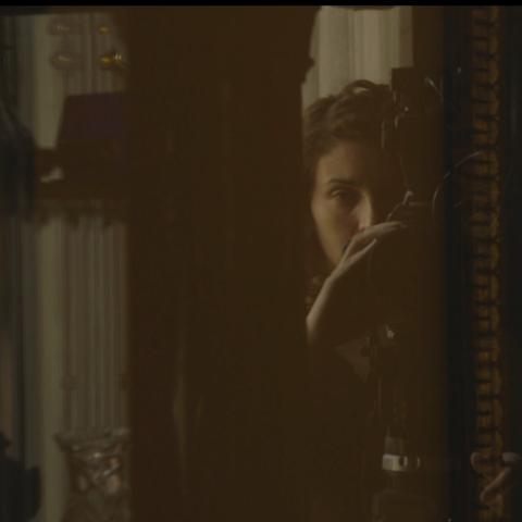 Slightly blurred view through a filmstrip on the face of a woman looking through the viewfinder of a film camera.
