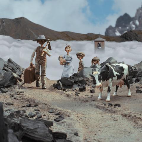 Ein Animationsfilmstill. Vier Puppenfiguren und eine Kuh stehen in einer steinigen Berglandschaft, hinter ihnen ist eine Schlucht voller Wolken, nur ein Kirchturm schaut heraus. Die Vaterfigur läuft mit Spitzhacke und Koffer in den Händen auf die Kamera zu, die Mutter mit Baby im Arm und zwei Jungen schauen ihm hinterher
