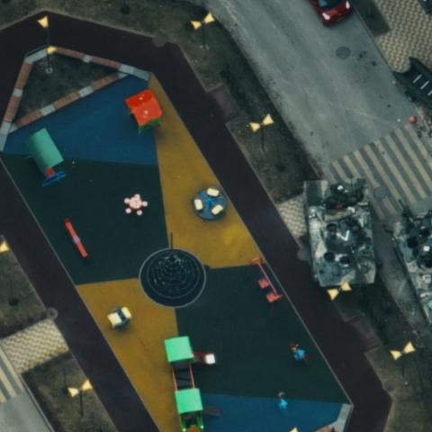 A bird’s eye view on a place in a city environment. Two tanks are crossing the place, a few cars are parking at the side. No people.