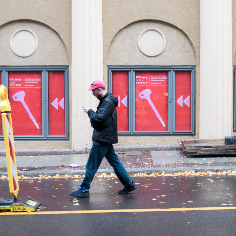 Ein Mann mit pinker Schirmmütze läuft über die Straße vor vielen Dok Plakaten