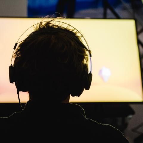 A person with headphones on looks at a brightly lit screen.