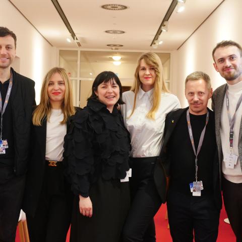 Six women and men in casual business attire stand side by side and smile at the camera.