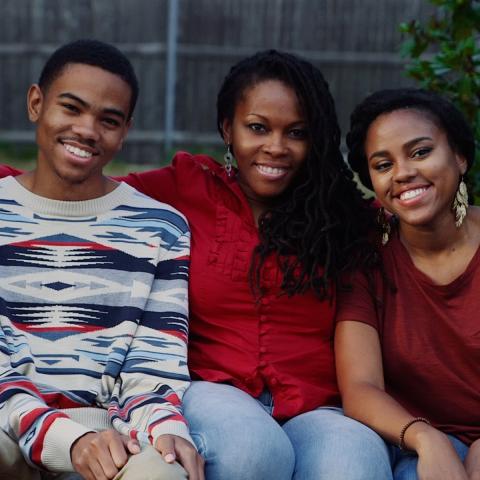Drei Schwarze Menschen sitzen nebeneinander auf einer Bank und lächeln in die Kamera.