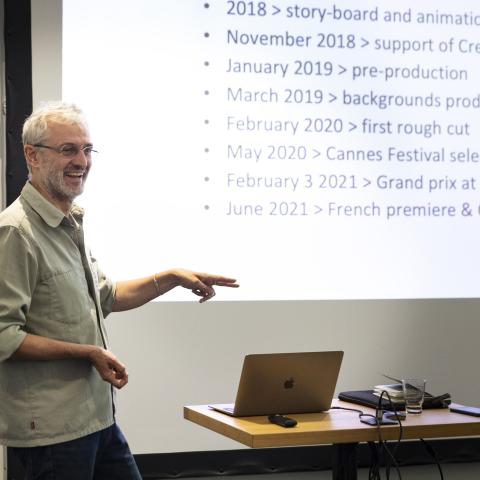 A man stands in front of a huge screen with a timeline on it. He smiles widely.