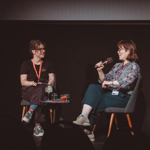 Franka Sachse and Tess Martin sit at a small coffee table and talk into microphones.