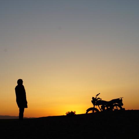 in front of a sunset, the silhouettes of a person and a motorbike are visible