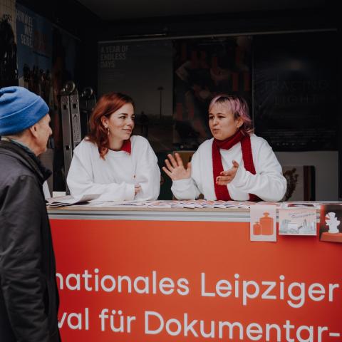zwei Volunteers stehen in der DOK Info Box und sprechen mit einem interessierten Passanten