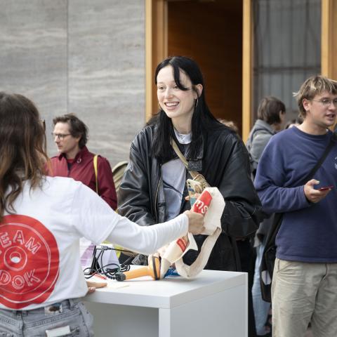 Volunteers überreicht einem Gast einen DOK Beutel 