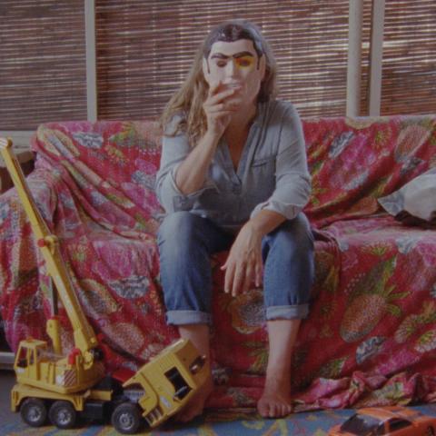 Lee Anne Schmitt is sitting on a sofa and holds a mask in front of her face