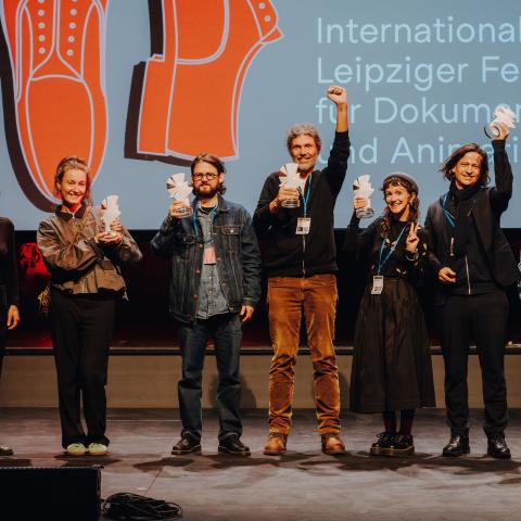 Gruppe von Personen auf Bühne, die ihre Tauben-Preise in die Luft halten