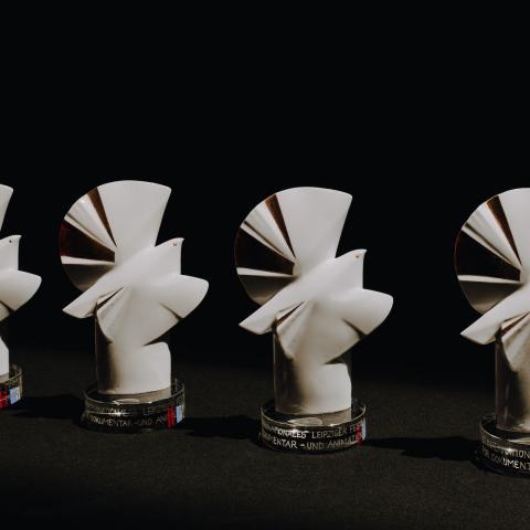 Vier Tauben-Trophäen aus Porzellan stehen nebeneinander auf einer dunklen Fläche, vor schwarzem Hintergrund.