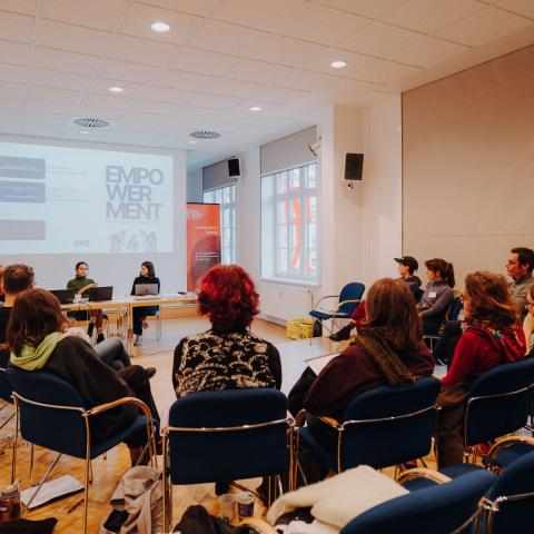 Ein Dutzend Menschen sitzen im Kreis in einem Seminarraum, vorne steht auf einer Leinwand das Wort Empowerment