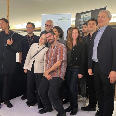 Group of film festival organisers on a stage; on the left, one person speaks into a microphone, with banners of international documentary markets behind them.