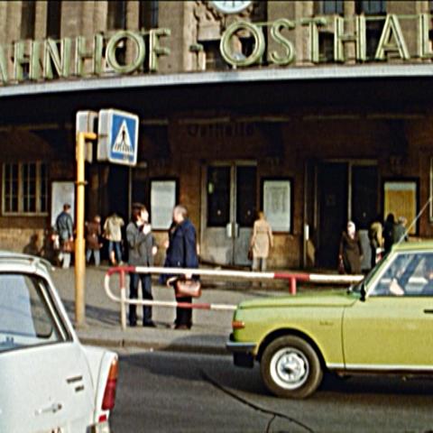 Analog wirkendes Bild vom Osteingang des Leipziger Hauptbahnhofs mit einem gelben Wartburg-Auto davor