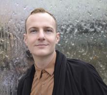 Portrait of Rob Eagle looking at the camera, with short hair and a piercing in one ear