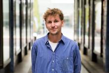Portrait picture of Lars Rummel. He wears a blue short with white stripes and smiles at the camera.