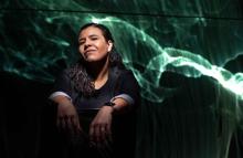 Portrait of Ana Monte in front of green light streaks on a black screen moving like waves