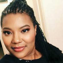 Toni is pictured indoors with neatly styled Sisterlocks, parted at the top and cascading gracefully over her shoulders.