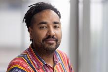Headshot of Heitor Augusto, a brown-skinned man, with dreadlocks and wearing a colorful, pinstripe shirt.