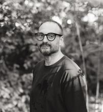 schwarz-weiß foto von einem mann mit brille, der in die kamera schaut