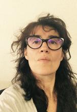 weiße Frau mit langen dunklen lockigen Haaren und großer Brille