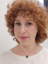 A portrait shot of woman in her thirties with curly red hair and blue eyes. She is smiling and looking directly into camera. 